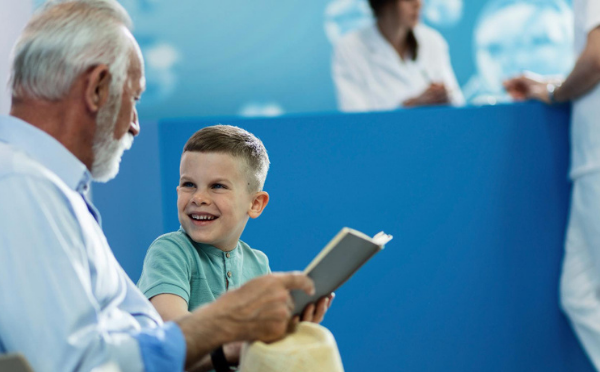 Menino feliz e seu avô lendo livro e se comunicando enquanto aguardam consulta médica na clínica
